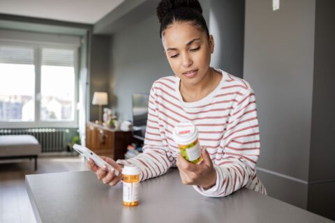 Woman holding phone and reading pill bottle