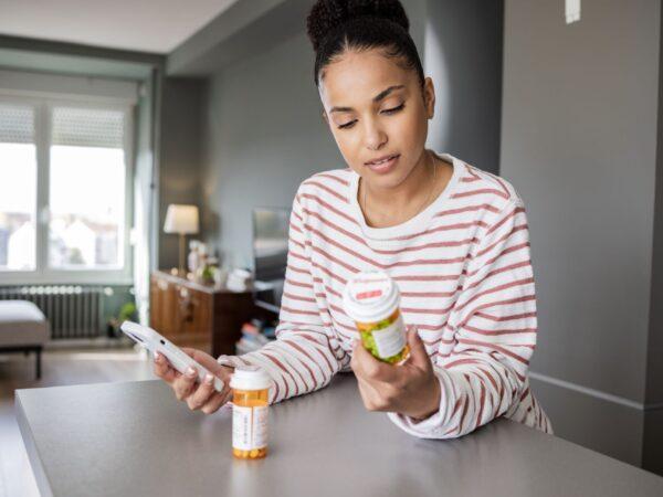 Woman holding phone and reading pill bottle