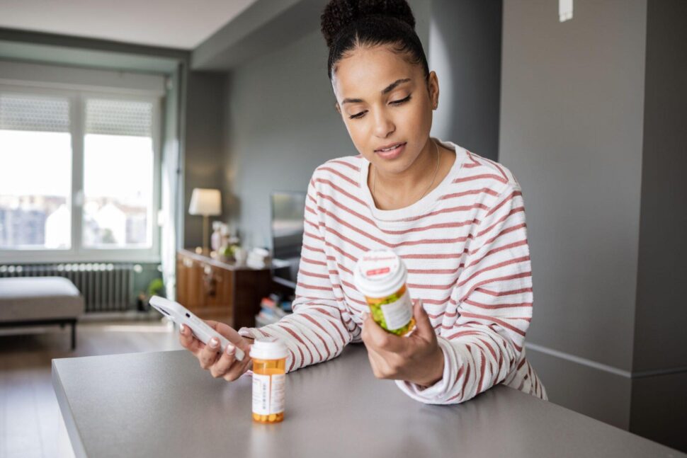 Woman holding phone and reading pill bottle