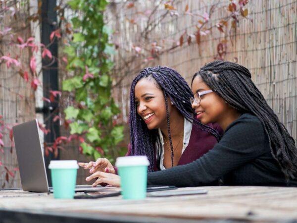 two friends with coffee cups working on a laptop