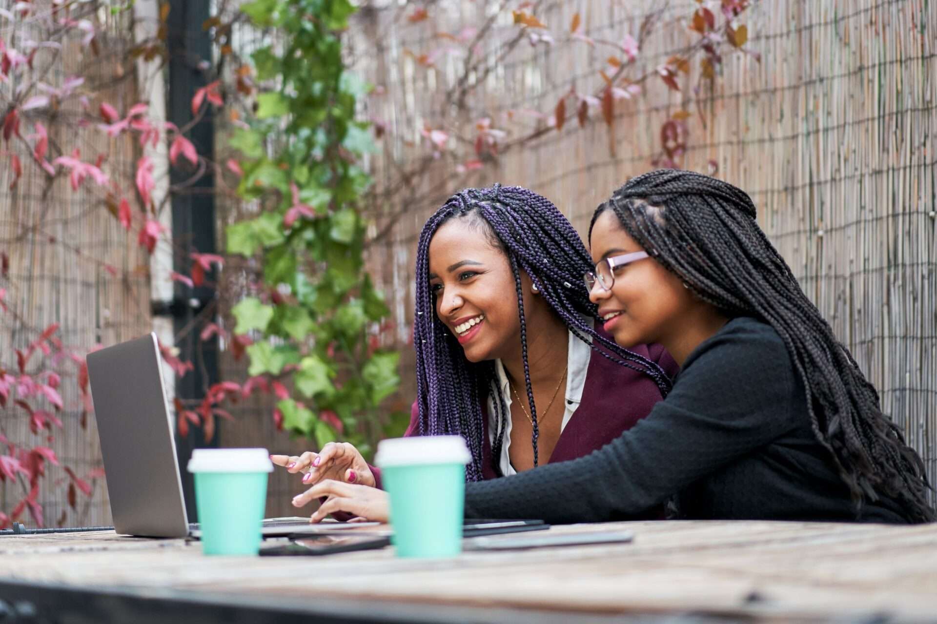 two friends with coffee cups working on a laptop